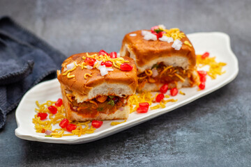 Dabeli is a spicy Indian street food made with a potato filling, tamarind chutney, and sev, served in a bun.