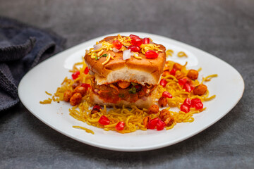 Dabeli is a spicy Indian street food made with a potato filling, tamarind chutney, and sev, served in a bun.