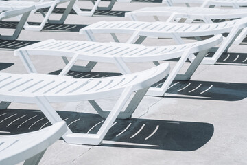 White lounge chairs arranged neatly around a sunlit pool area showcasing geometric patterns and shadows during the afternoon