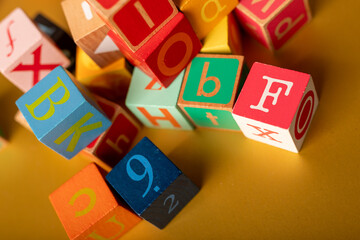 A jumbled pile of colorful alphabet blocks on a yellow surface The letter F is in focus
