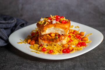 Dabeli is a spicy Indian street food made with a potato filling, tamarind chutney, and sev, served in a bun.