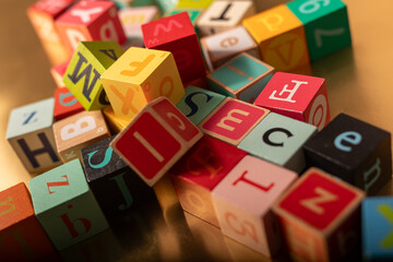Obraz premium Colorful wooden blocks spelling out letters of the alphabet scattered on a gold surface