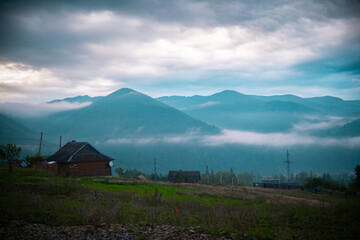 Misty mountains surround a tranquil village at dawn with fog rolling through the valleys and soft light illuminating the landscape