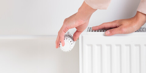 A woman adjusting the temperature on a heating radiator, focusing on saving money and conserving energy