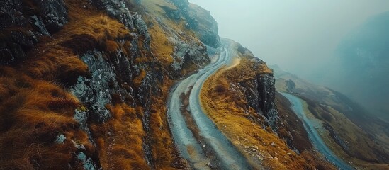 Naklejka premium Winding mountain road snaking through a majestic awe inspiring landscape of towering rocky cliffs deep canyons and dramatic geological formations This remote