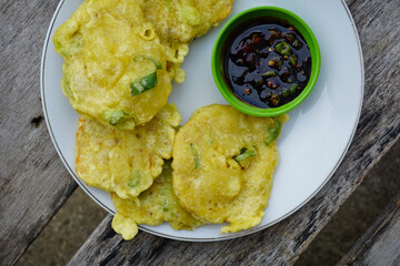 Delicious Indonesian fried tempeh mendoan is served on a white plate with savory dipping sauce on a...