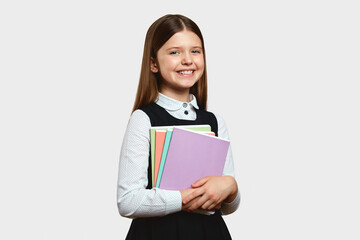 Cheerful active excellent student girl holding books and copybooks in both hands wearing school uniform, isolated over white background