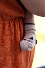 A portrait of the cute leg and foot of a baby wearing a cosy sock pressed safely against the caring mother who is carying the small child.