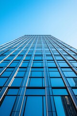 A tall skyscraper with numerous reflective windows extends into the clear blue sky, showcasing modern architecture and design.