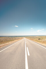 Stunning image of a long, open road stretching into the horizon under a clear blue sky, embodying the spirit of travel and adventure. The scenic countryside setting evokes a sense of freedom 