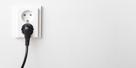A close-up of a double electrical outlet mounted on a white wall, with a power cord plugged into one of the sockets, banner