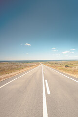 Naklejka premium Stunning image of a long, open road stretching into the horizon under a clear blue sky, embodying the spirit of travel and adventure. The scenic countryside setting evokes a sense of freedom.