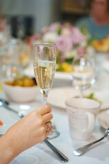 A glass of white wine in a woman's hand with a ring on her ring finger. The tradition of making toasts on holidays.