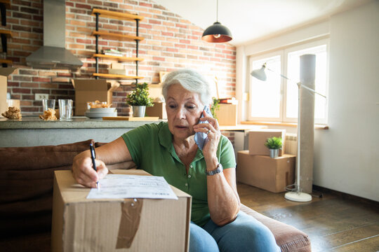 Senior woman on phone while labeling moving boxes in new home