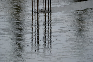 Raindrops on the surface of the puddle. Rainy day. Reflection of a reinforcing bar in a puddle of...