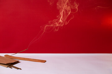 An incense stick smokes on a red background