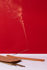 An incense stick smokes on a red background
