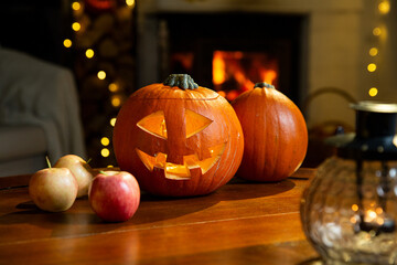 Halloween pumpkin jack-o'-lantern on old wooden table with burning fire place background in a living room on the eve of Halloween, holiday vibes