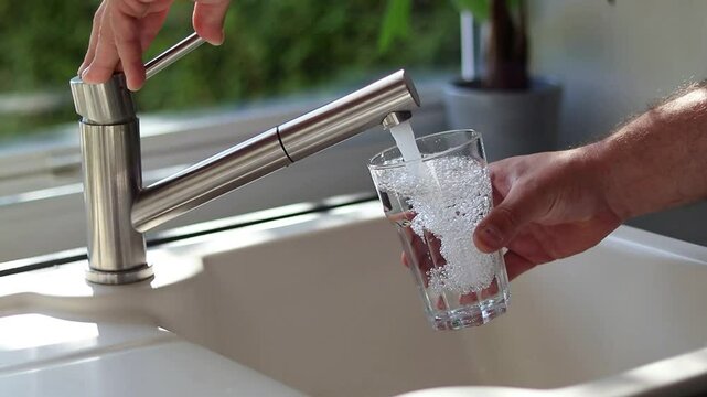 Close up of male hands pouring tap water into a glass in the kitchen