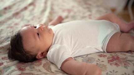 Baby resting on bed, relaxed expression, observing surroundings with curiosity in a comfortable home environment, showcasing calmness, peace, and connection