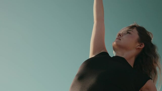 A young woman performs an abstract dance move outdoors against a clear blue sky, embodying grace and expression.