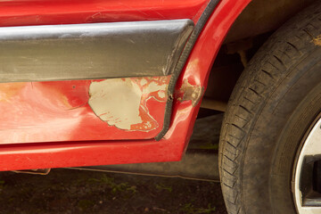 red car door damage or dent closer to the rear wheel close-up, due to side collision or parking...