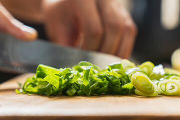 slicing fresh green onions with chef's knife, in a wooden board