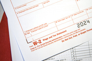 Wage and Tax statement form W-2 in red color with American flag in the backdrop.