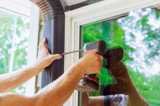 Handyman is assembling gutter channel that is attached to roof with installation of gutter