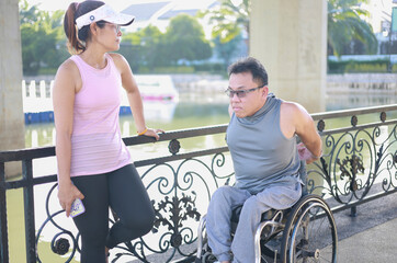 Obraz premium Asian disabled person sits in a wheelchair with a friend pushing in a city park and exercises for good health, having fun in the gentle spring sunshine.