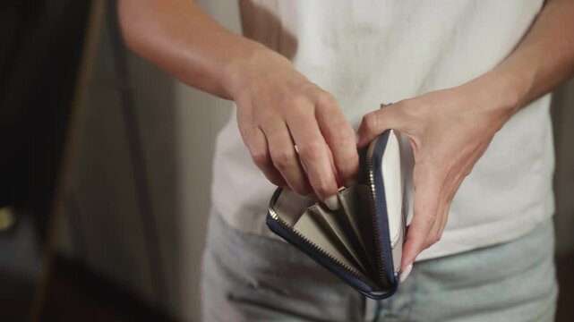 Woman opens her wallet, revealing emptiness inside. She pulls out a twenty-dollar bill, highlighting the absence of cash and the challenges of financial struggles