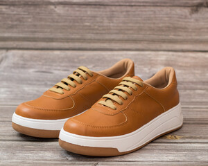 Casual style sneakers, light brown and white on a wooden background, profile view