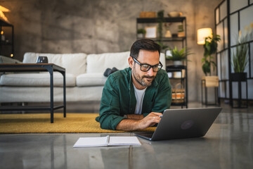 Adult man work from home lying down on the floor with laptop computer