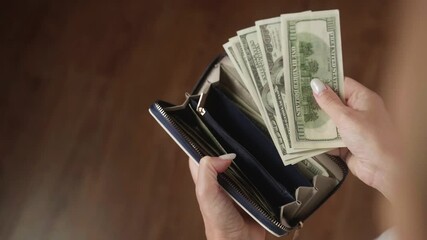 Woman counting 100 us dollar bills while holding a leather wallet. The scene captures the essence of managing cash and reflects themes of finance and wealth