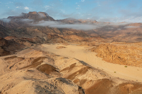 Aerial view of The dry bed of the Ugab river cuts through arid desert plains, behing the Brandberg, Namibia's highest mountain, aerial view, drone shot, Damaraland, Namibia.