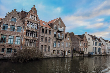 Naklejka premium Historic brick buildings along the canal in Ghent showcase the city's architectural charm during a calm afternoon