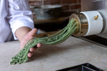 Chef prepares green noodles using a pasta machine in a trendy kitchen at a downtown restaurant 