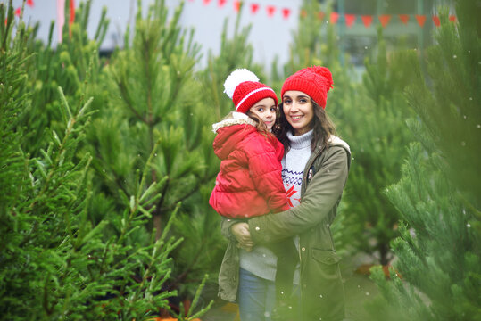 mother holds her daughter in her arms against the backdrop of many Christmas trees and snow.