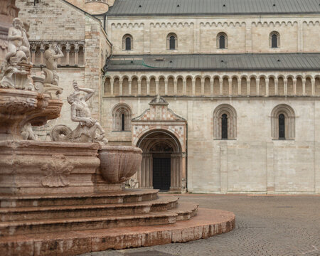 View of historic cathedral and ornate fountain in a cobblestone square, Trento, Italy.