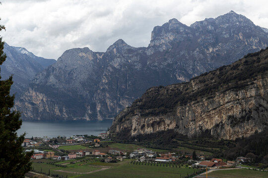 View of serene Lago di Garda surrounded by majestic mountains and a picturesque village, Riva del Garda, Italy.