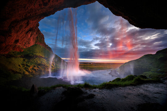 View of seljalandsfoss waterfall surrounded by lush greenery and dramatic cliffs at sunset, Seljalandsfoss, Iceland.