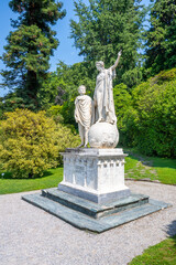 Obraz premium In the lush gardens of Villa Melzi, the statue of Dante and Beatrice stands elegantly, surrounded by vibrant greenery and pathways, embodying a scene of literary romance and art.
