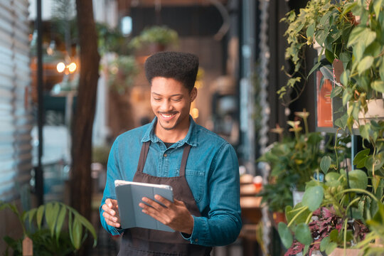 African American barista in flower shop using tablet.Smiling man in apron checking orders on mobile device