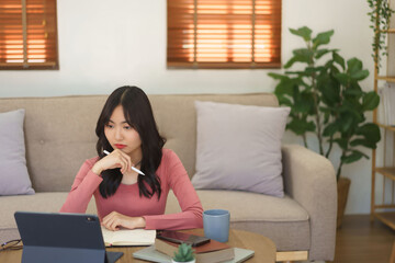 Young businesswoman holding pen stylus and concentrated with reading business report on tablet