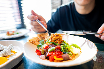person enjoying a meal with a plate of colorful food, including vegetables and meat, in a cozy dining setting. image captures the moment of eating, emphasizing the vibrant and appetizing presentation.