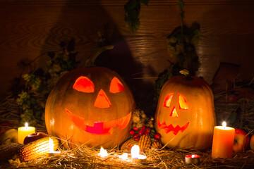 pair of halloween jack-o-lantern pumpkin among dry grass, burning candle, fruits  and leaves in dark
