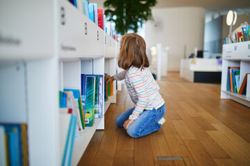 Five year old girl selecting a book in municipal library
