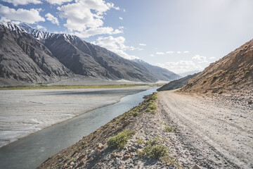 Dusty Pamir Highway road winds along the Panj River in the Wakhan Corridor in the Tien Shan Mountains of Tajikistan