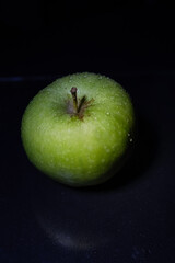 Green juicy apple with water drops on dark background. Still life.