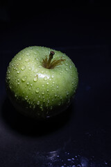 Green juicy apple with water drops on dark background. Still life.